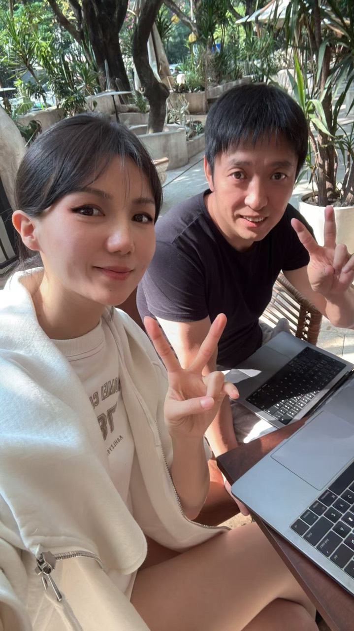 Miranda 和 Yan 在树荫下的户外咖啡店一起比耶自拍,桌上放着笔记本电脑